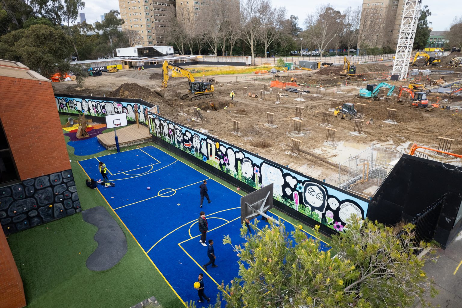 Aerial view of mural on a wall that separates a primary school basketball court with the housing development